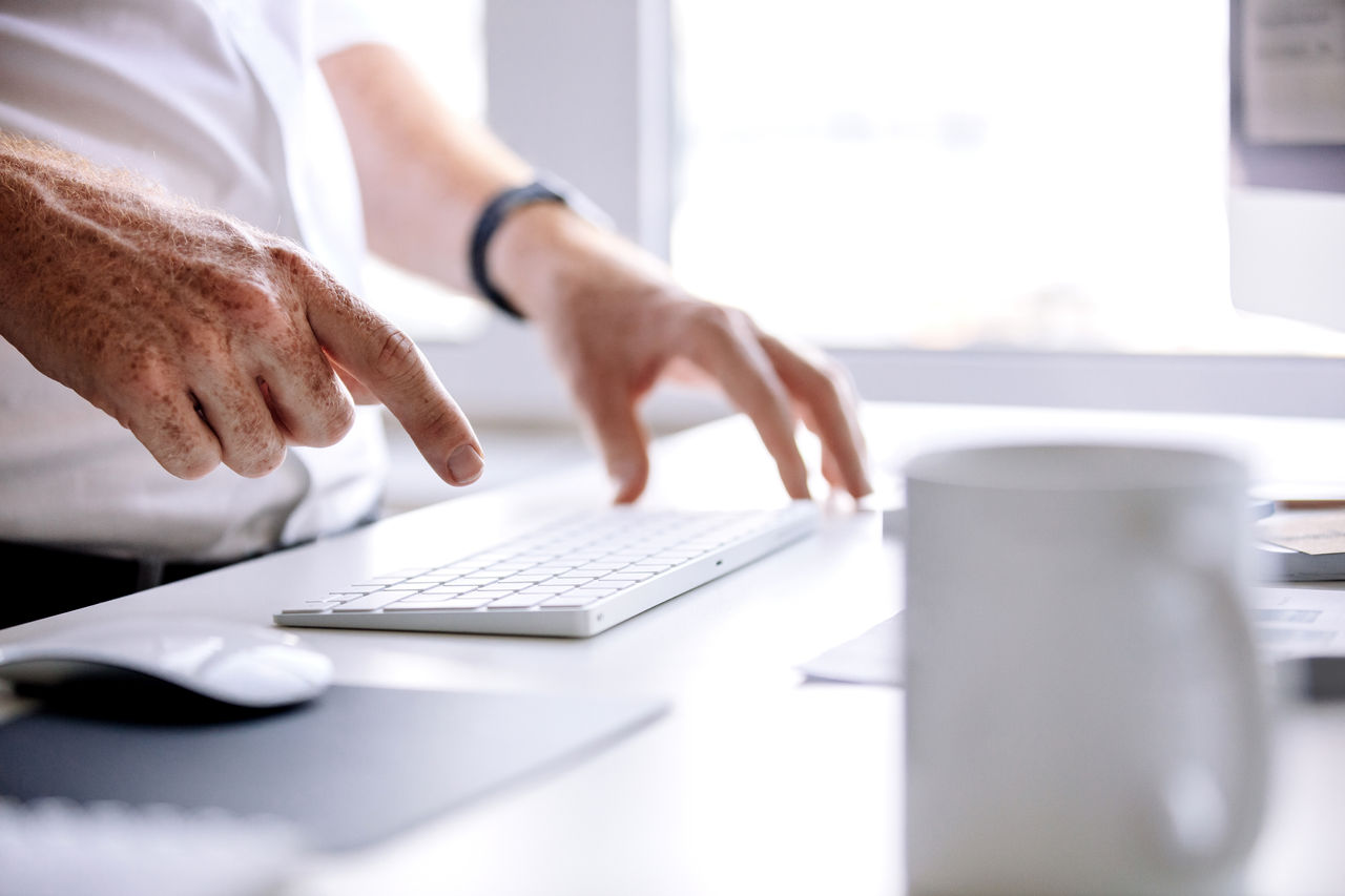 Close up shot of young man hands typing on wireless keyboard on desk in office.