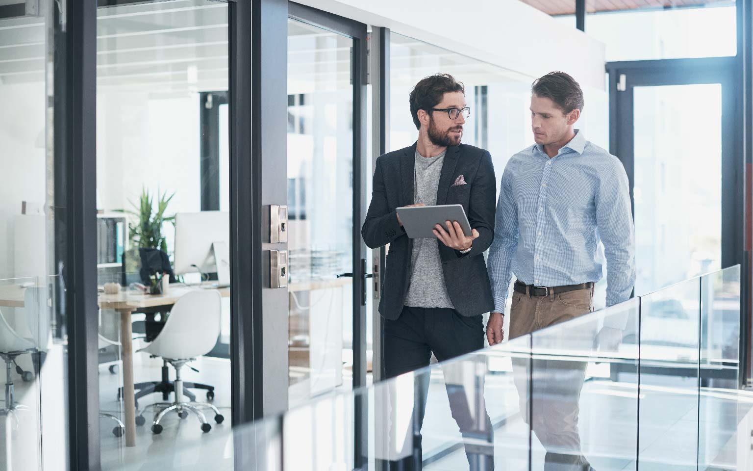 two businessmen walking in office corridor holding a tablet