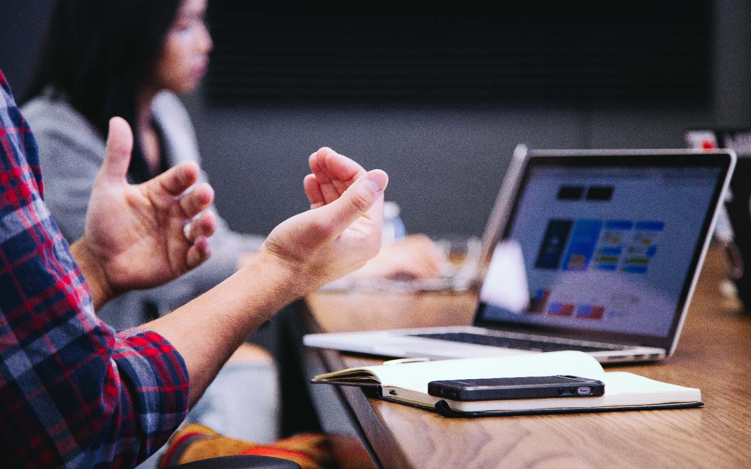 A person sitting at a table with laptop computer making hand gesture